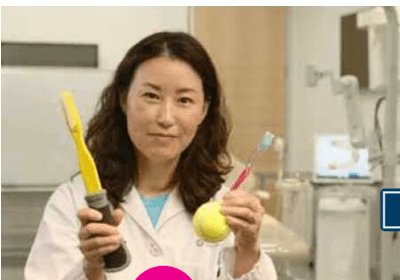 A woman holding two toothbrushes and an orange.