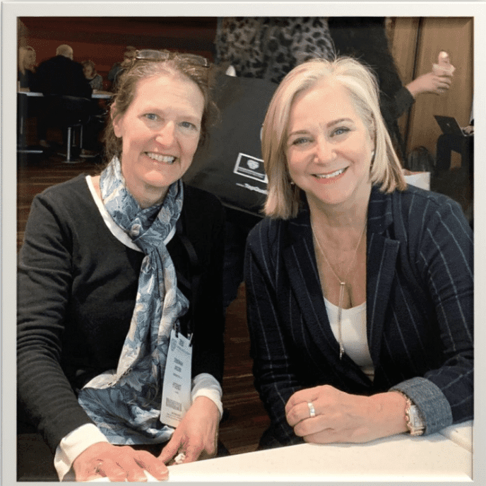 Two women sitting at a table smiling for the camera.