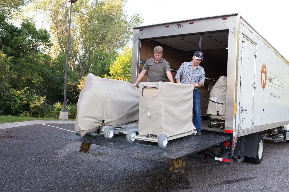 Two men unloading a truck with furniture on the back.