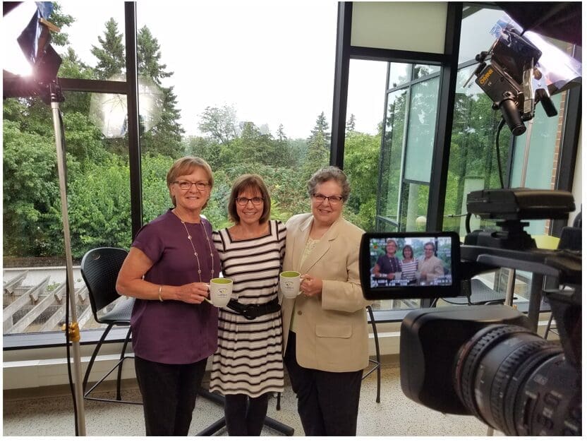 Three women standing in a room with a camera.